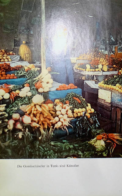 found book page, color photography print of a vegetable stand in tunis. the shop owner face is flashed by the camera, in the background there are pictures hanging on the wall