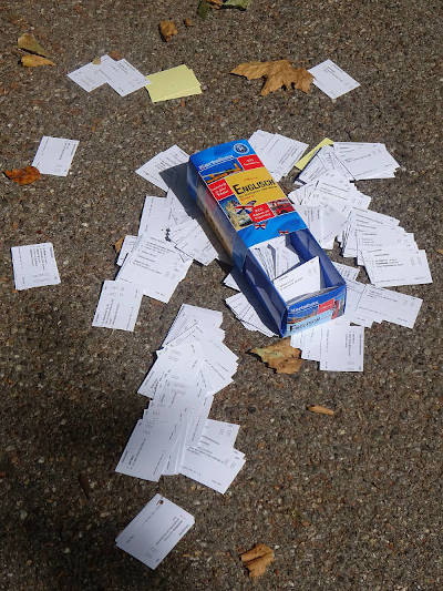 An open box of English vocabulary study cards is lying in the middle of the road. The cards are spread out on the asphalt.