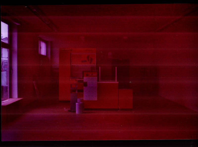 An abandoned post office. An empty counter stands alone in the room. Photography with old analogue film, scan lines.